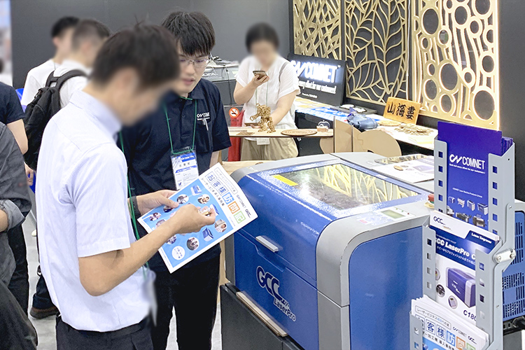 コムネット株式会社、サイン&ディスプレイショウ2019（SIGN&DISPLAY SHOW 2019）出展中の様子：レーザー加工機導入事例冊子をご覧いただきながら、GCC社製レーザーカッターC180のデモンストレーション